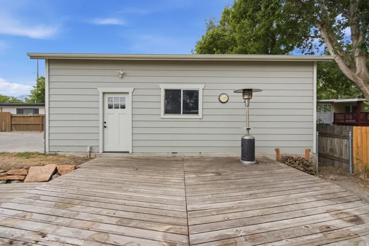 Wood-decked patio with light-toned siding, a white exterior door with window panes, and a single window with white trim