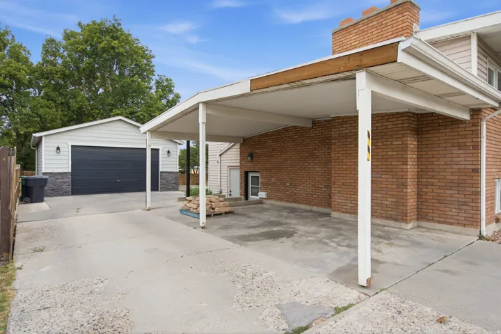 Carport with concrete driveway, brick exterior, and detached two-car garage featuring a dark panel door
