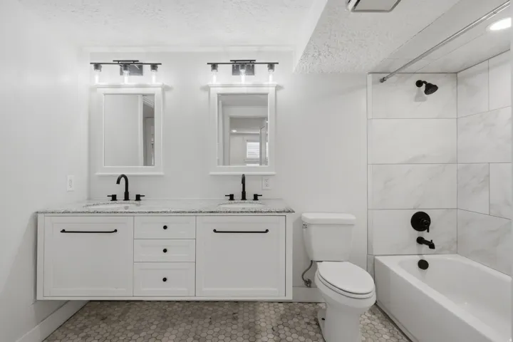 Dual vanity with granite-style countertop, matte black fixtures, and white cabinetry