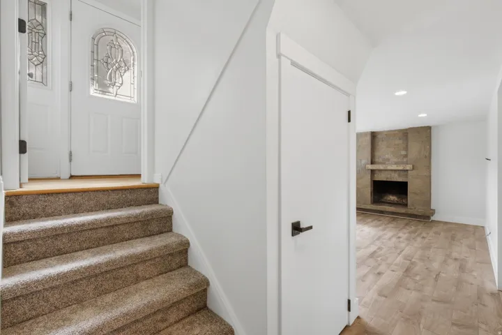 Carpeted stairs with white risers, wood-finish flooring, stone fireplace surround, modern white door, and recessed lighting