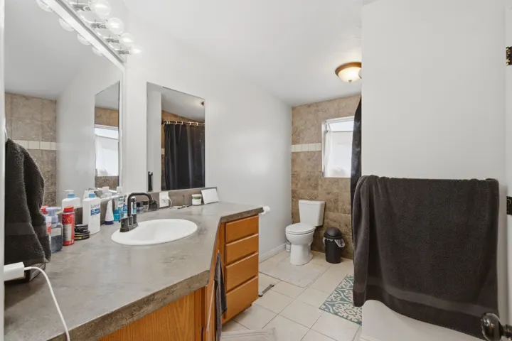 Single vanity with an integrated sink, dark countertop, wood-finish cabinetry, and a wall-mounted mirror