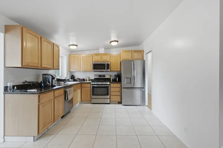 Kitchen featuring wood-finish cabinetry, stainless steel appliances, dark countertops, and tile flooring