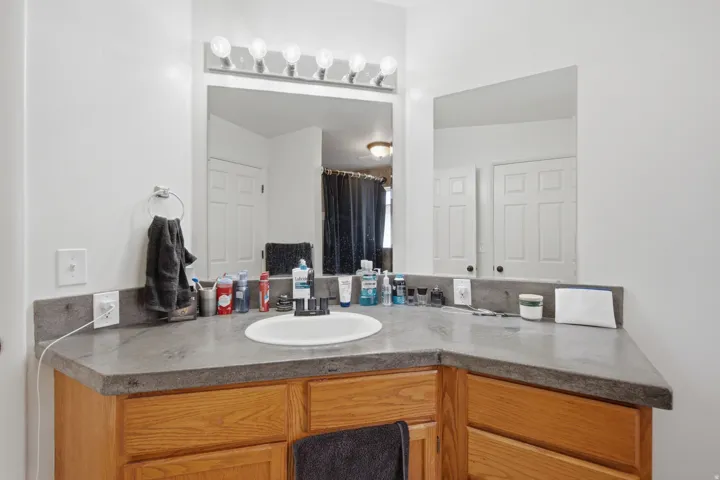 Vanity with light wood-finish cabinetry, solid surface countertop, integrated sink, mirrored wall, and overhead strip lighting