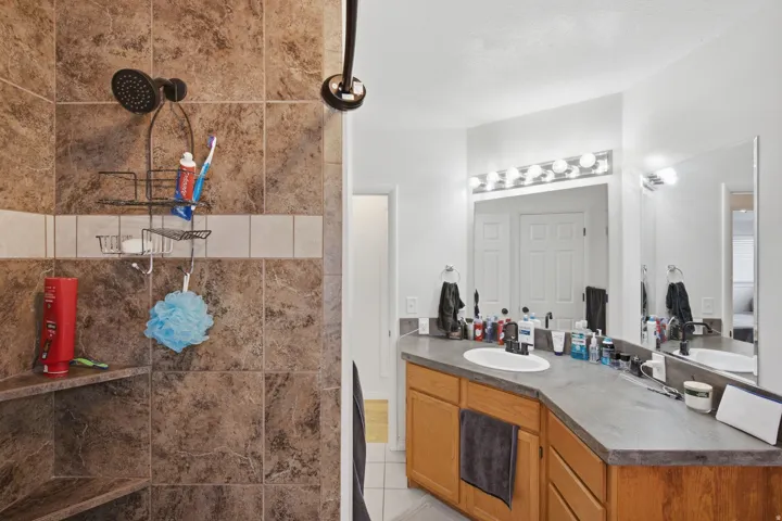 Tiled shower with corner shelving, bronze-finish shower fixtures, wood-finish vanity, integrated sink, and vanity mirror with sconce lighting