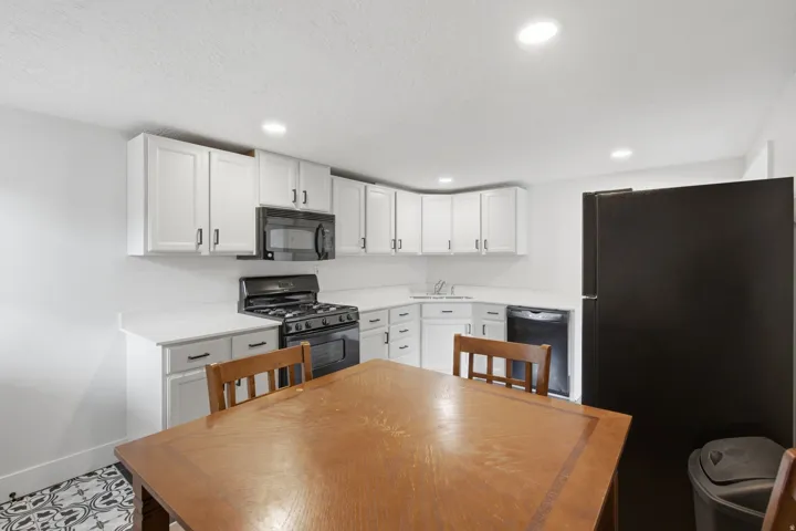 White shaker cabinetry, black appliances, recessed lighting, and patterned floor tile