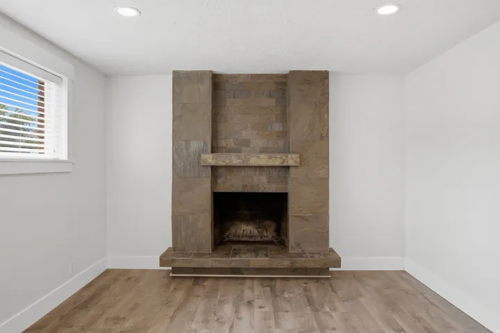 Stone-clad fireplace with a hearth, wood-finish flooring, recessed lighting, and a window with blinds