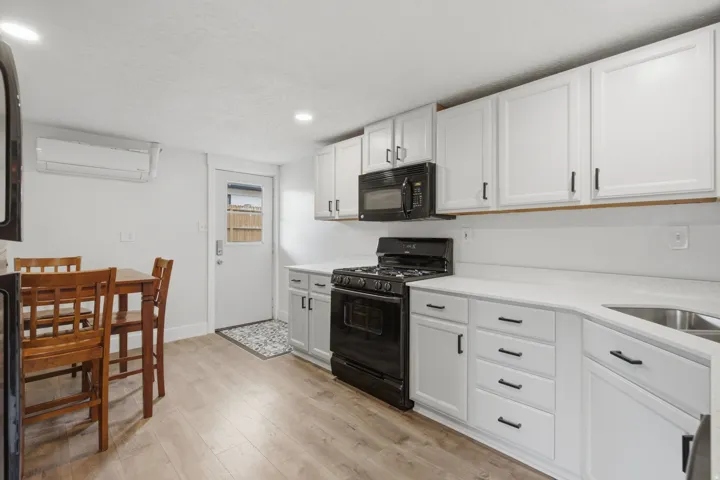 Light-toned wood-finish flooring, white cabinetry with black hardware, black appliances, white countertops, and a stainless steel sink