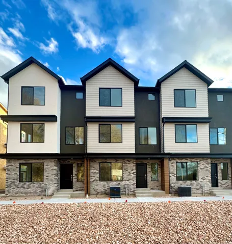 Modern townhome exterior with mixed material facade, featuring light-toned siding, dark stucco, and a brick base