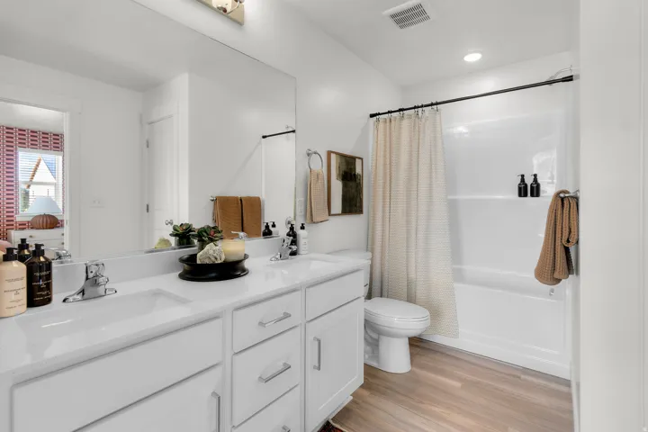 Double vanity with undermount sinks and white cabinetry, expansive mirror, wood-finish flooring, and a white tub/shower combination