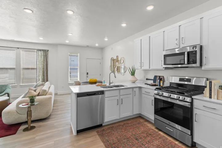 Open-concept living space featuring a kitchen with stainless steel appliances, white cabinetry, and light-toned countertops