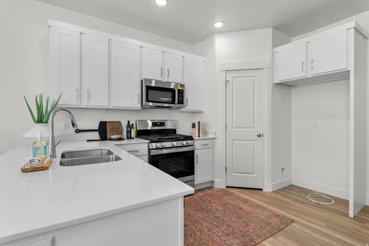 Kitchen featuring white shaker cabinetry, stainless steel appliances, light-toned countertops, a dual basin sink with a gooseneck faucet, and wood-finish flooring