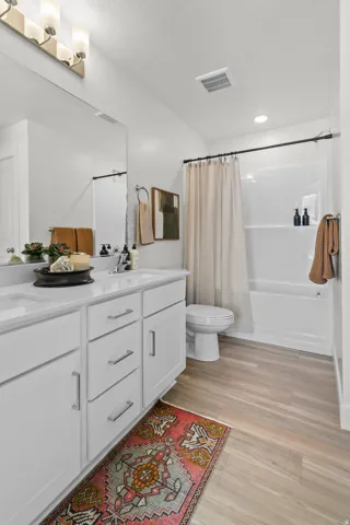Spacious bathroom featuring a double vanity with undermount sinks, wood-finish flooring, a full bathtub with shower, and recessed lighting