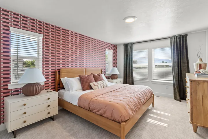 Patterned accent wall, light wood-finish bed frame, multiple windows, recessed ceiling light, and carpet flooring