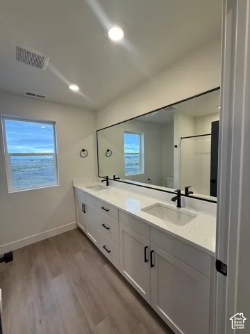 Double vanity featuring white cabinetry, quartz countertops, undermount sinks, matte black hardware, and wood-finish flooring