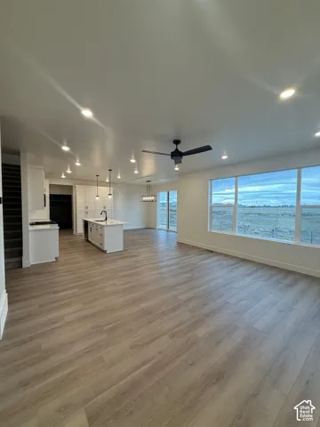 Open-concept area featuring wood-finish flooring, recessed lighting, a center kitchen island with a basin sink, and large windows