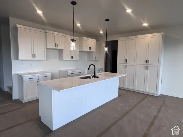 Kitchen featuring white shaker-style cabinetry, a large center island with a sink, pendant lighting, recessed ceiling lights, and stone countertops