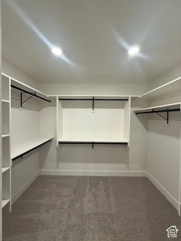Walk-in closet featuring white built-in shelving, multi-level hanging rods, recessed ceiling lighting, and wall-to-wall carpeting