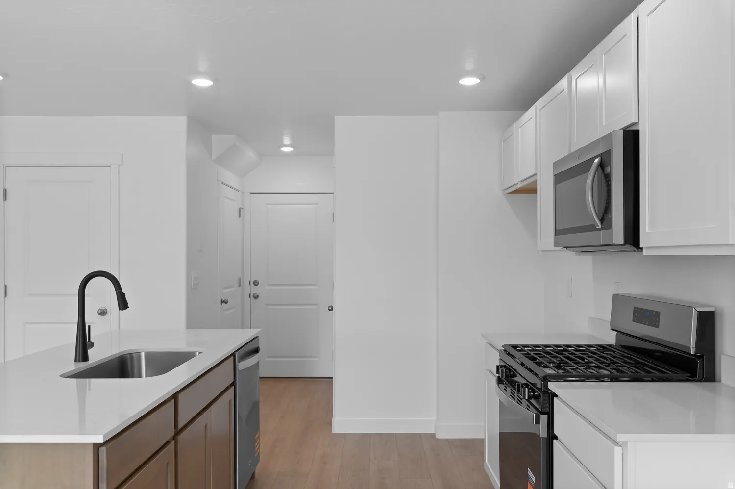 Kitchen featuring white cabinetry, stainless steel appliances, a kitchen island with sink, and wood-finish flooring
