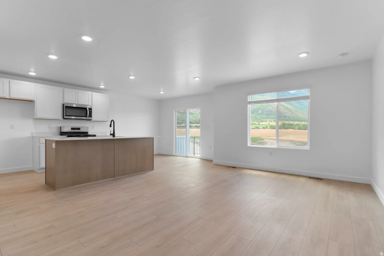 Expansive open-concept space featuring recessed lighting, wood-finish flooring, and a kitchen with white cabinetry and a wood-finish island