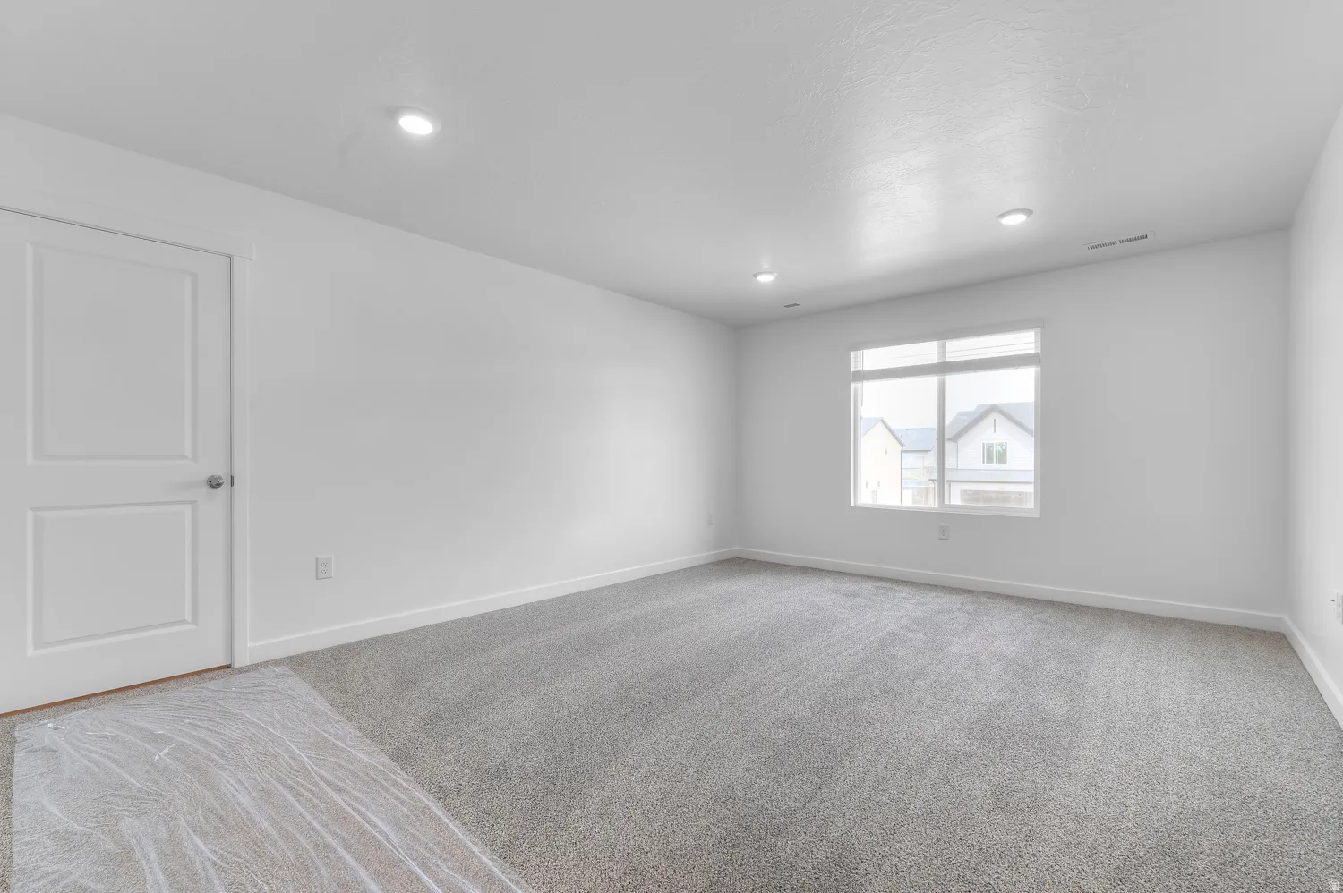 Recessed ceiling lighting, white interior door with polished hardware, large window with white frame, grey carpet flooring, and white painted walls