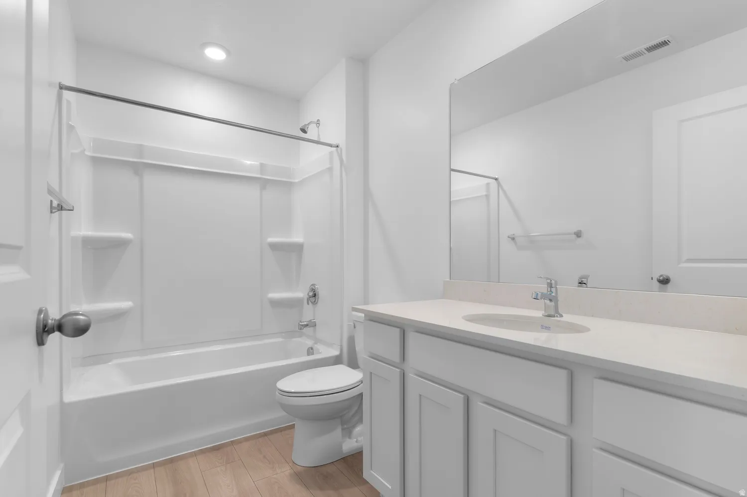 Bathroom featuring a built-in tub with an integrated shower, white vanity with an undermount sink, reflective mirror, and wood-finish flooring