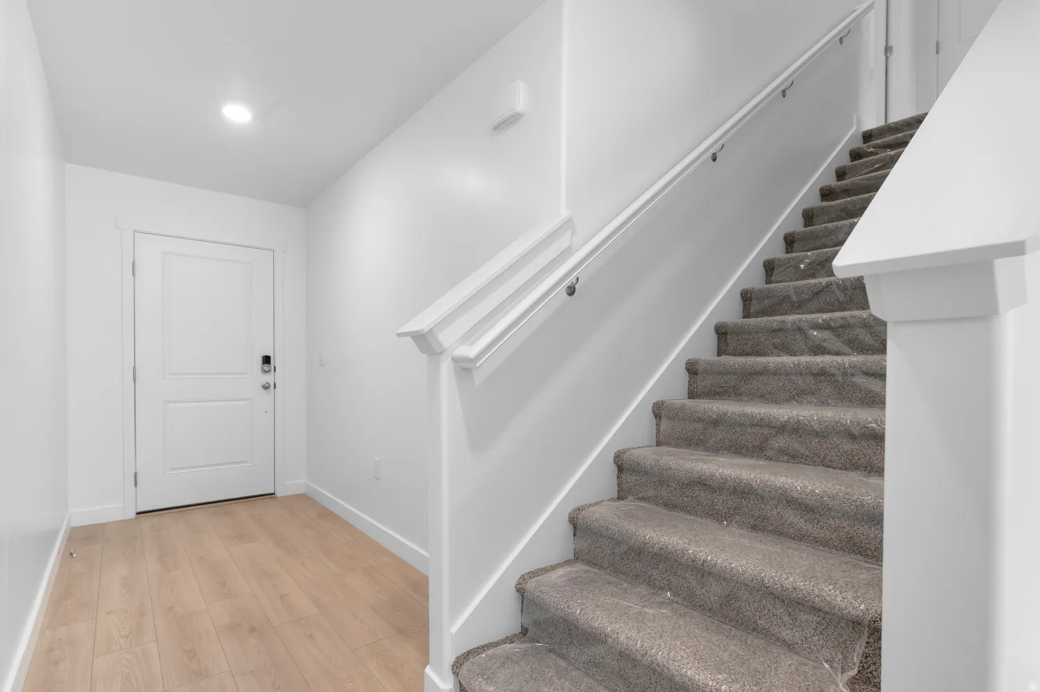 Wood-finish flooring, recessed ceiling lighting, two-panel interior door, and carpeted staircase with white handrail