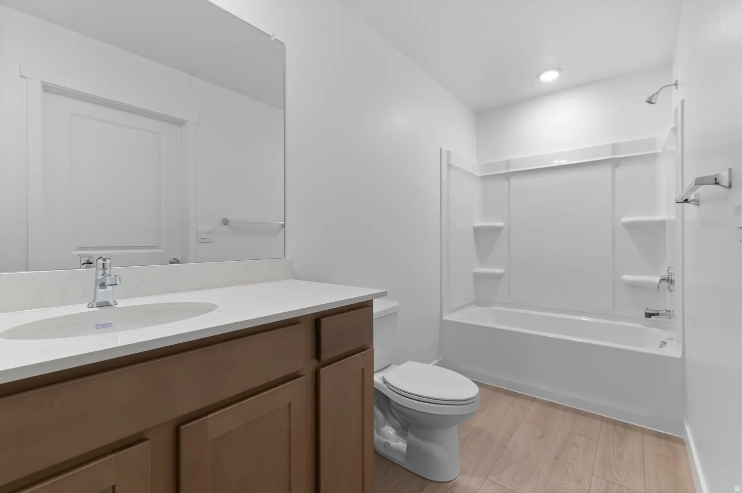 Wood-finish flooring, white walls, built-in vanity with light countertop, chrome fixtures, and a shower/tub combination