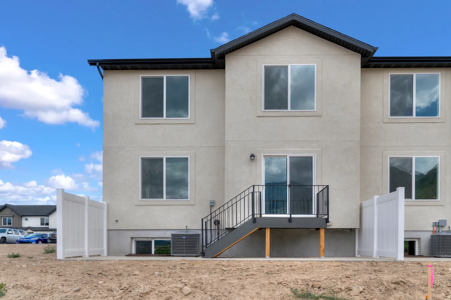 Light beige stucco exterior with black trim, multiple windows, and a sliding glass door leading to a deck with black railings