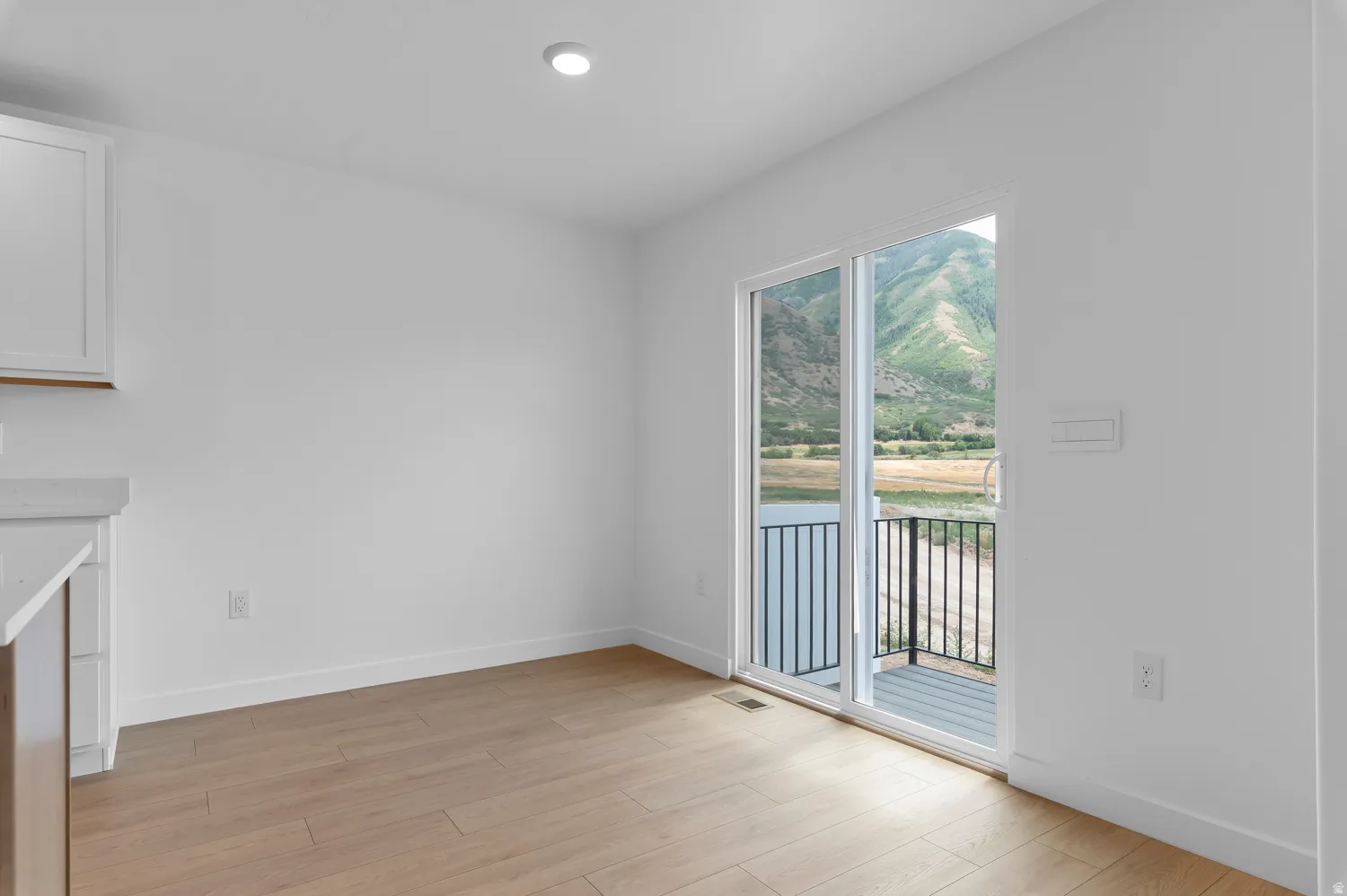 Wood-finish flooring, recessed lighting, white walls, and a sliding glass door leading to a balcony with mountain scenery