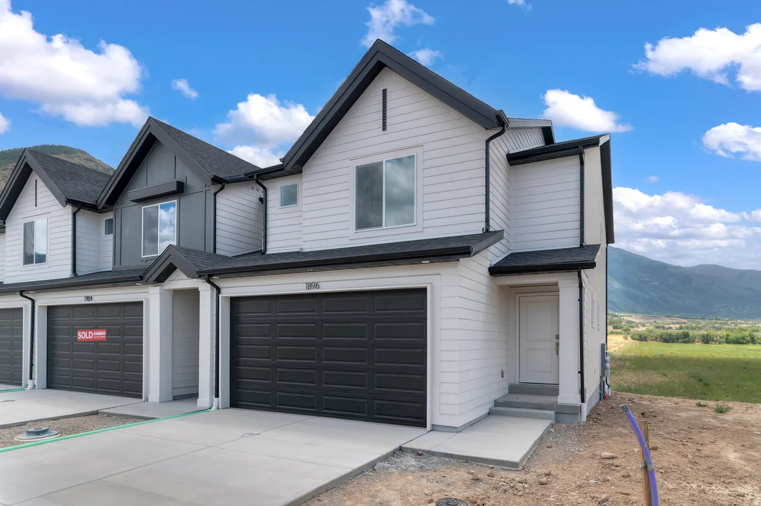 Modern townhome exterior with light-colored horizontal siding, dark asphalt shingles, and an attached garage with a dark panel door