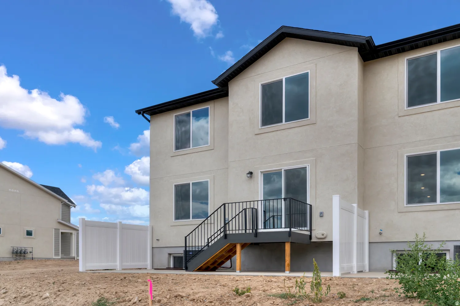 Stucco exterior with multiple windows, a rear deck with black metal railings, and a white vinyl privacy fence