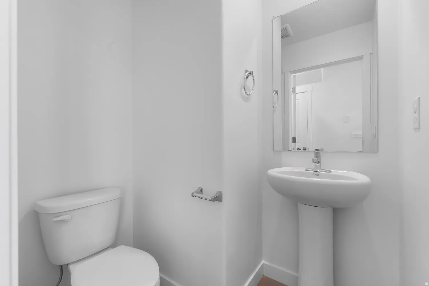 Pedestal sink with chrome faucet, wall-mounted mirror, and white toilet
