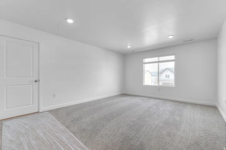 Recessed ceiling lighting, white interior door with polished hardware, large window with white frame, grey carpet flooring, and white painted walls