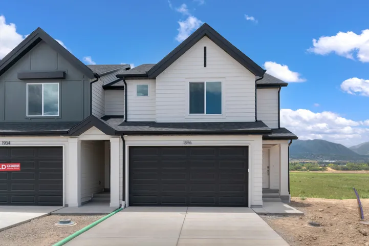Modern townhome with white siding, a black roof, attached garage, and a concrete driveway