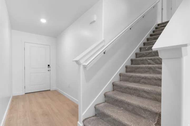 Wood-finish flooring, recessed ceiling lighting, two-panel interior door, and carpeted staircase with white handrail