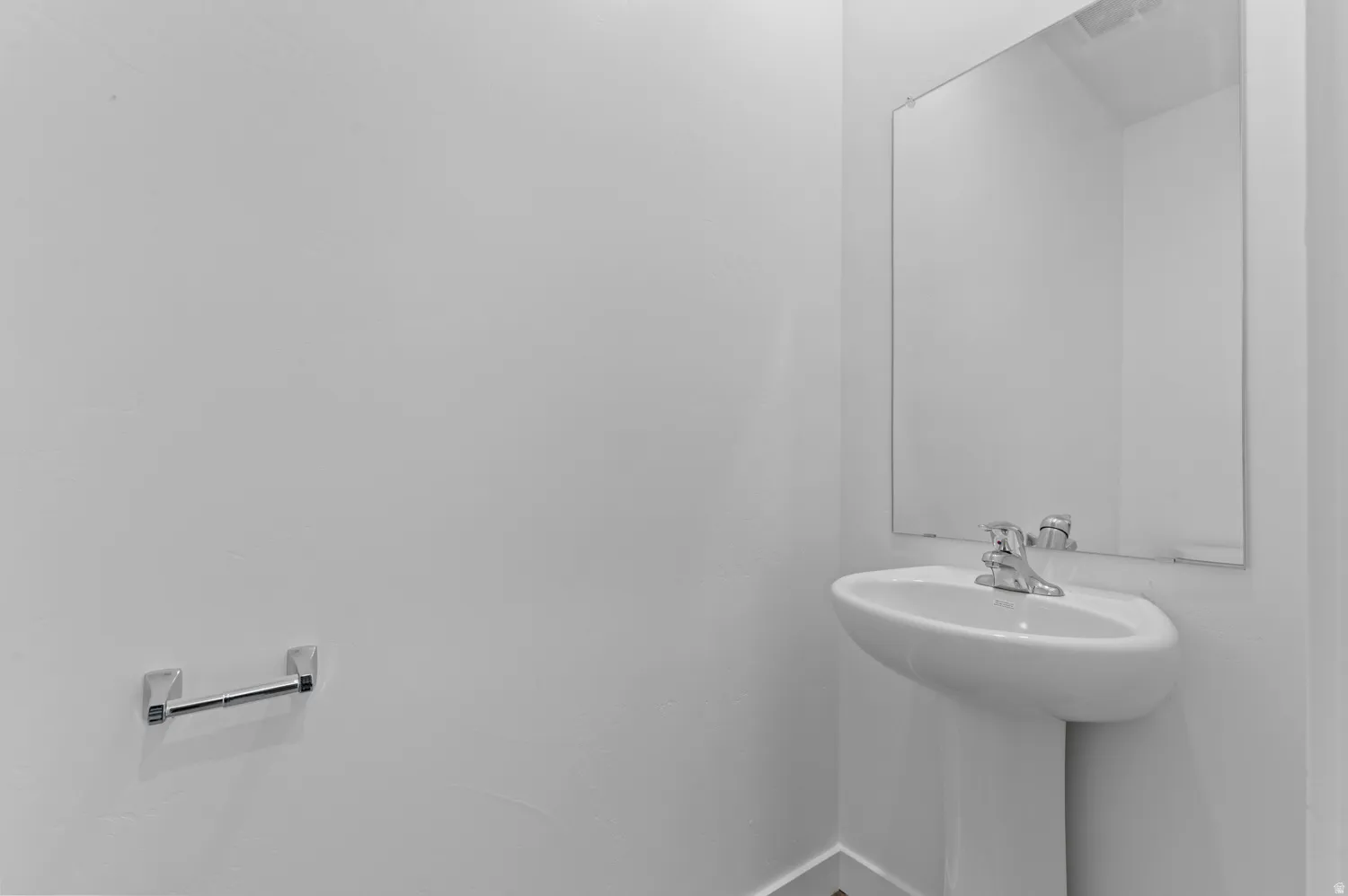 Pedestal sink with chrome faucet, wall-mounted mirror, and wall-mounted towel bar