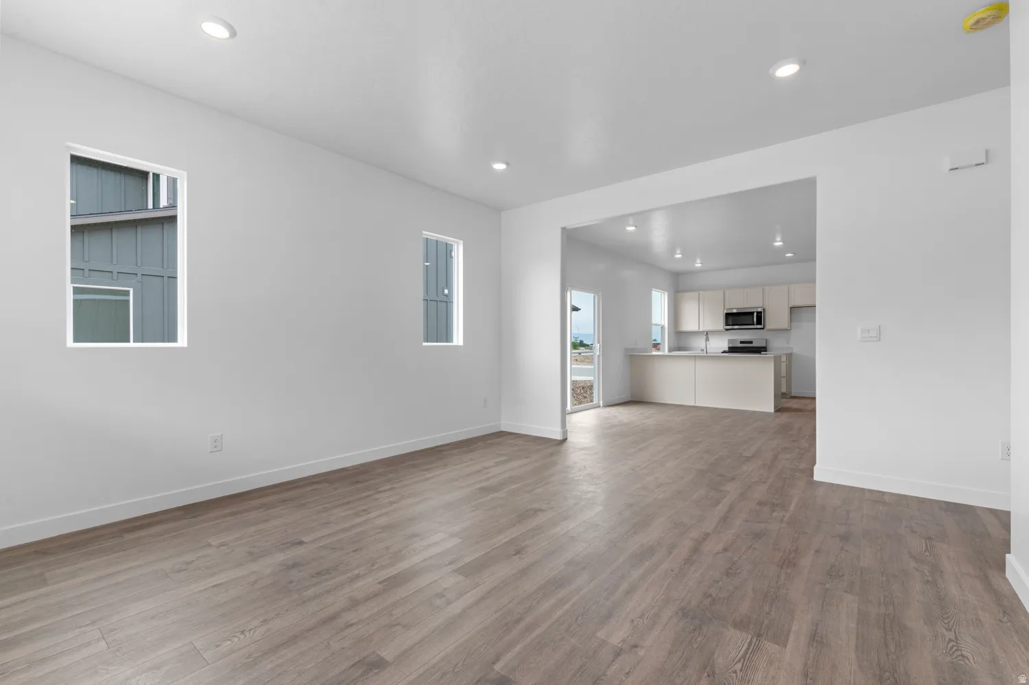 Recessed lighting, wood-finish flooring, white walls, and a kitchen with stainless steel appliances and light-toned cabinetry