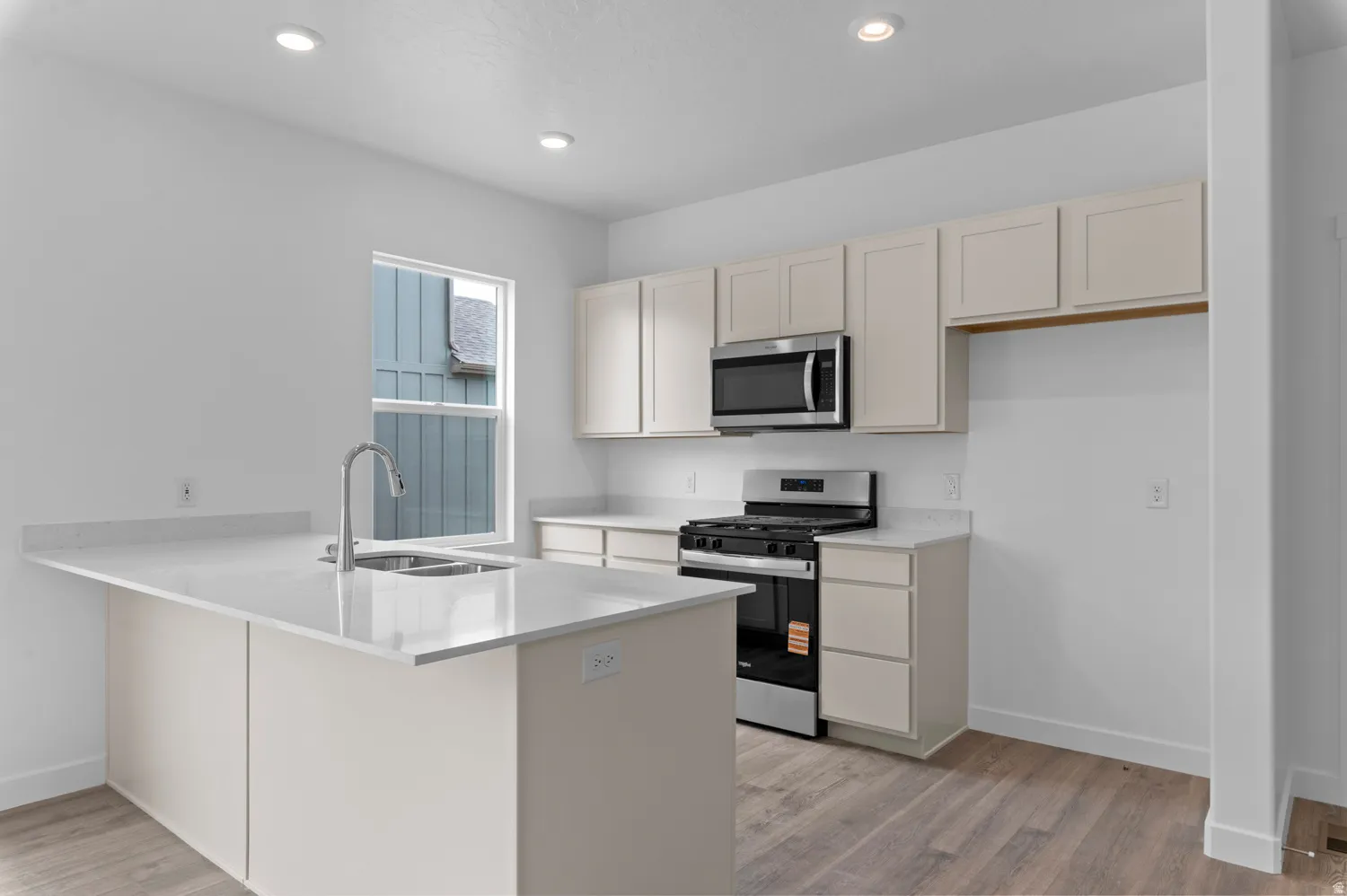 Kitchen featuring light cabinetry, stainless steel appliances, recessed lighting, and wood-finish flooring