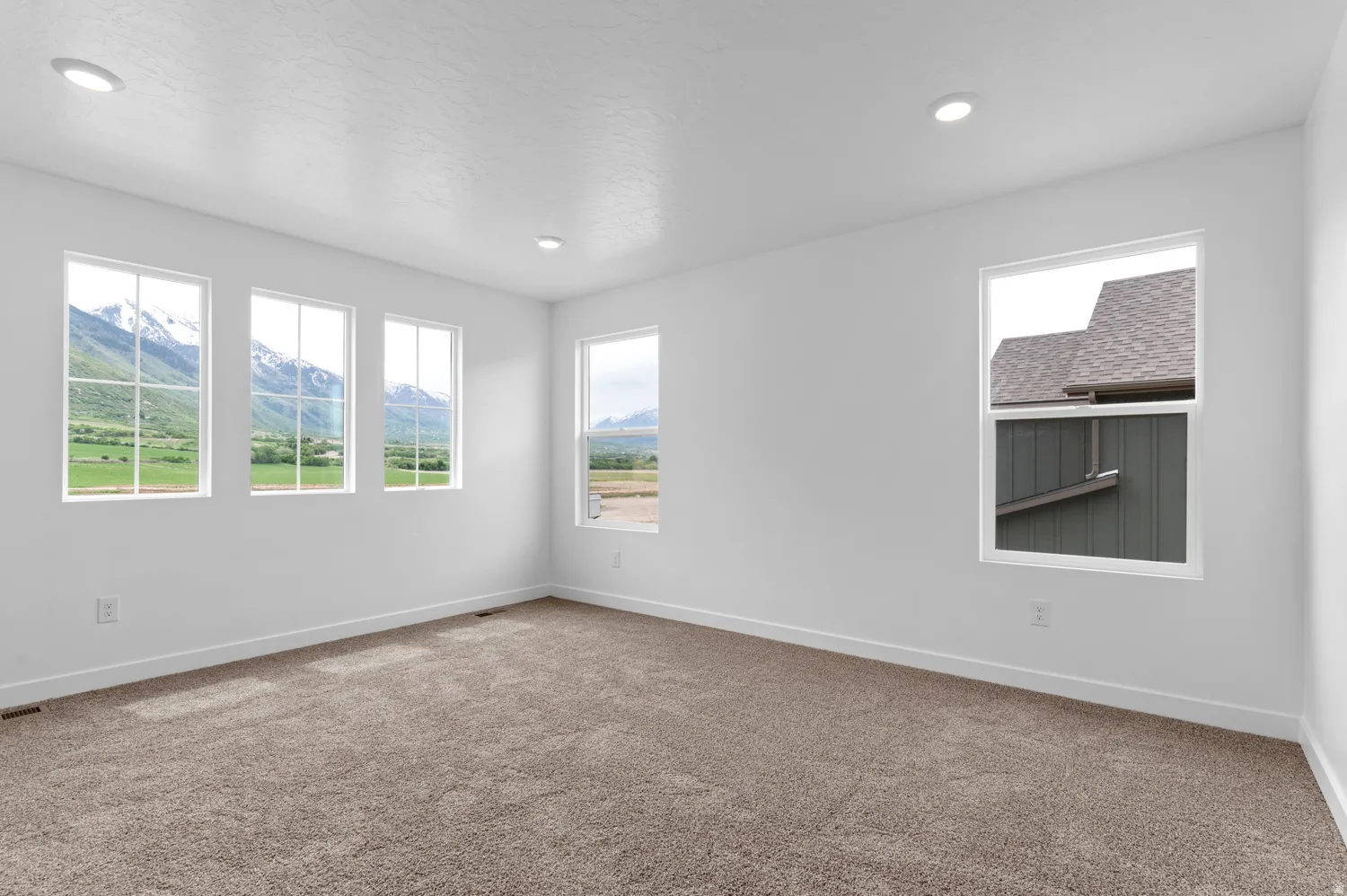 Recessed ceiling lighting, white walls, multiple windows, broad baseboards, and neutral carpet