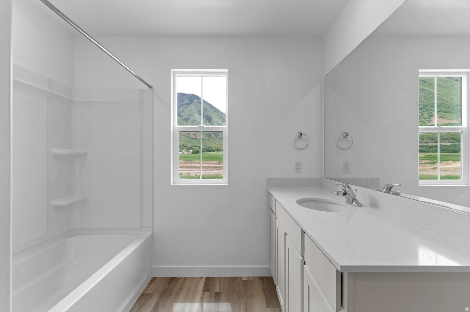 White bathtub with integrated shower, single vanity with light-colored countertop, integrated sink, and chrome faucet