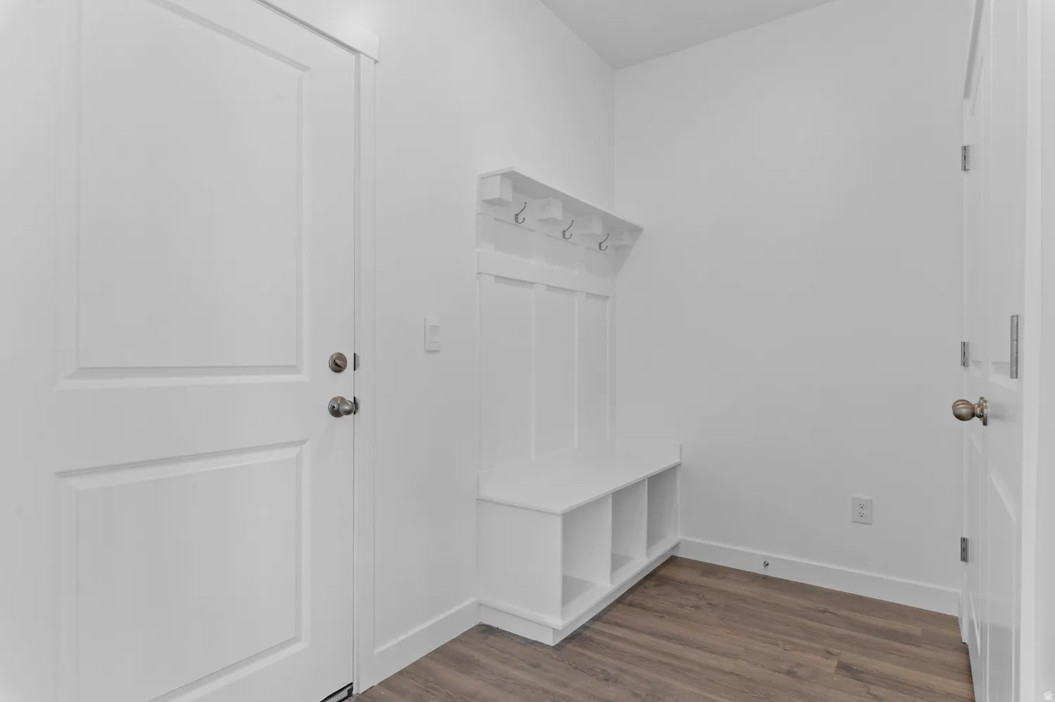 Built-in bench with storage cubbies and coat hooks, wood-finish flooring, and white paneled doors