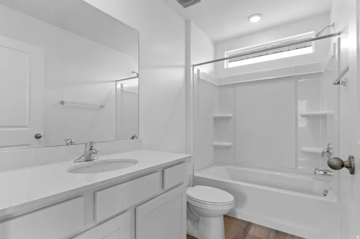 Bathroom featuring a vanity with an integrated sink, a large mirror, a shower/tub combination with a white surround, and wood-finish flooring