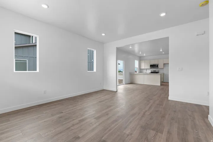 Recessed lighting, wood-finish flooring, white walls, and a kitchen with stainless steel appliances and light-toned cabinetry