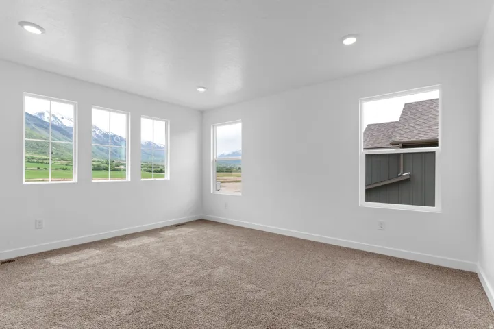 Recessed ceiling lighting, white walls, multiple windows, broad baseboards, and neutral carpet