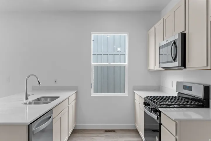 Kitchen featuring light-toned cabinetry, stainless steel appliances, a double basin sink, light countertops, and wood-finish flooring