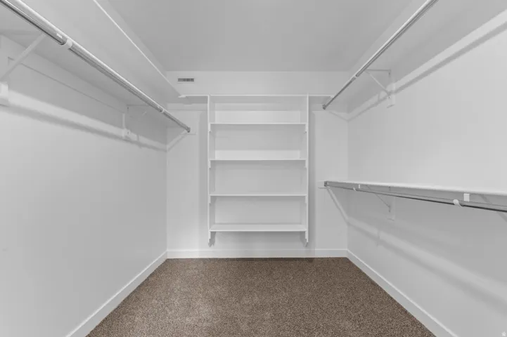 Walk-in closet featuring white walls, white shelving, metal hanging rods, and carpet flooring