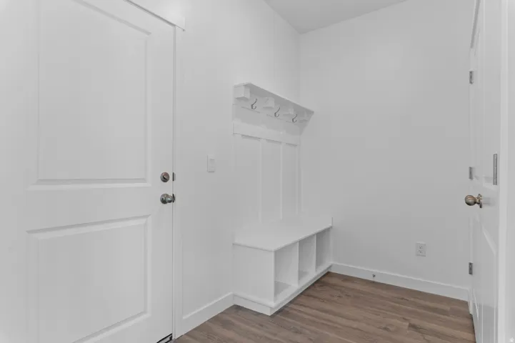 Built-in bench with storage cubbies and coat hooks, wood-finish flooring, and white paneled doors
