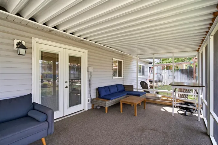 Covered patio with a corrugated ceiling, wall-mounted light fixture, and double glass-paneled doors