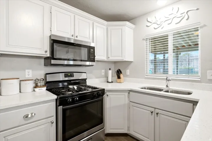 White cabinetry, stainless steel appliances, dual basin sink, white countertops, and wood-finish flooring