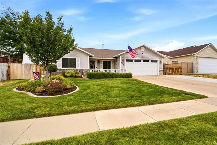 Siding exterior with stone accents, attached garage, concrete driveway, and landscaped front yard with a tree and shrubbery